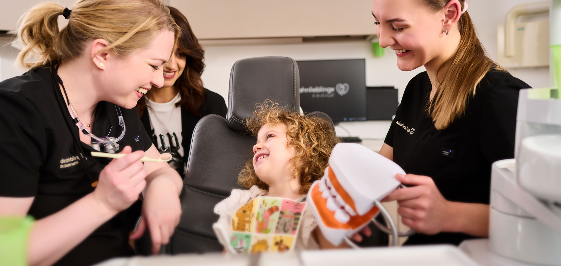Als Kinderzahnärztin der Zahnarztpraxis zahnlieblinge lacht Dr. Reuschl gemeinsam mit einem jungen Mädchen und ihrer Zahnassistentin