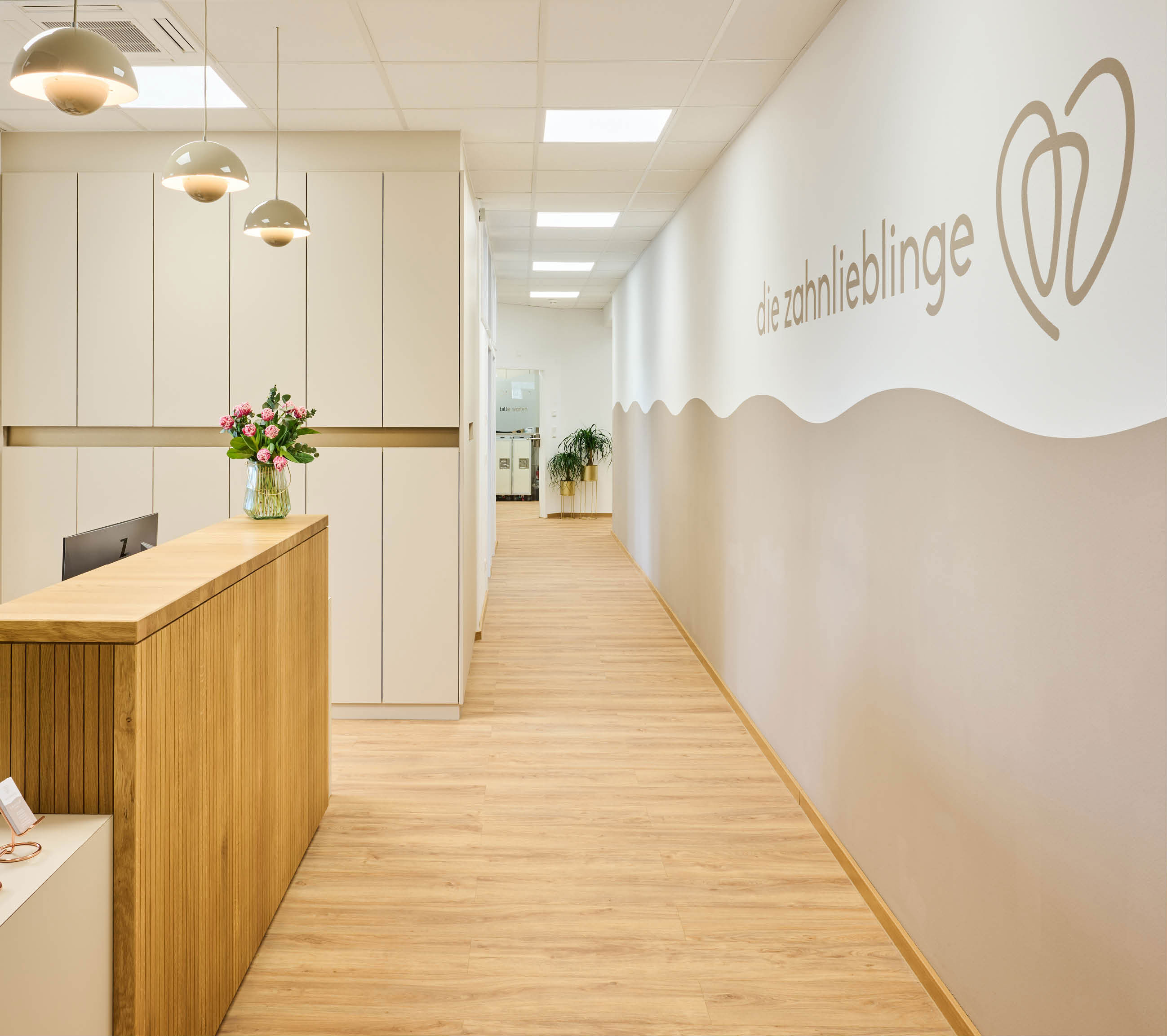 Der helle, einladende Empfangsbereich der Zahnarztpraxis Zahnlieblinge in Nürnberg mit einem Holztresen, beigen Wänden und sanfter Beleuchtung