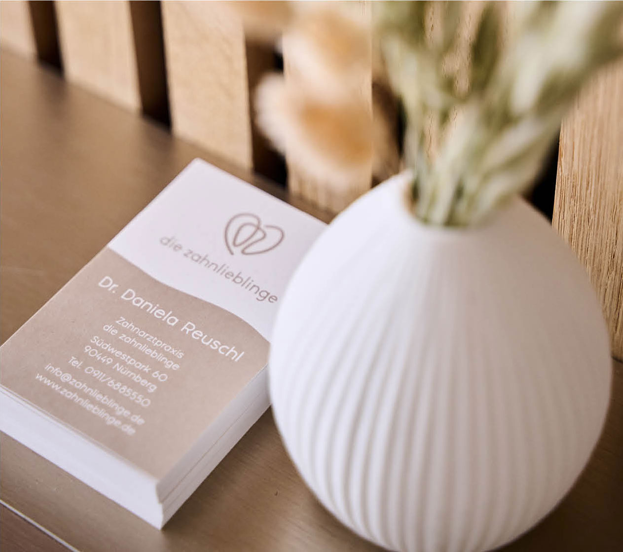 Im Eingangsbereich der Nürnberger Zahnarztpraxis liegen einige Flyer von Zahnärztin Dr. Reuschl neben einer weißen Vase mit Trockenblumen