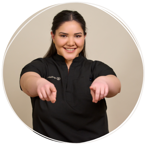 Oezlem Aykas, zahnmedizinische Fachangestellte bei Zahnärztin Dr. Reuschl und den zahnlieblingen, steht vor einem beigen Hintergrund und zeigt mit den Fingern in die Kamera